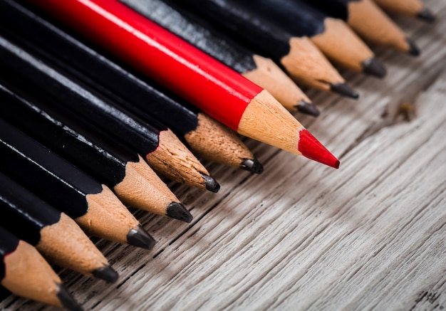 Red pencil stands out from the crowd of black  on a wooden white table