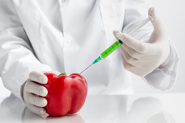 Red pepper on the desk with syringe filled with chemicals