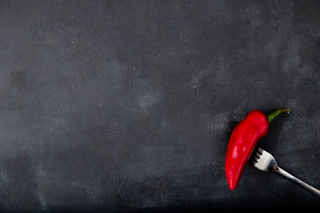 red pepper on fork on right side and black table