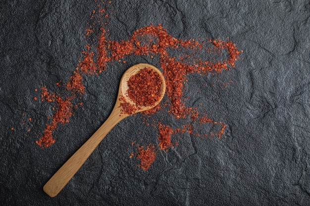 Red peppercorns with wooden spoon on black background.