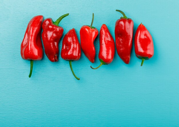 Red peppers on blue wall, top view.