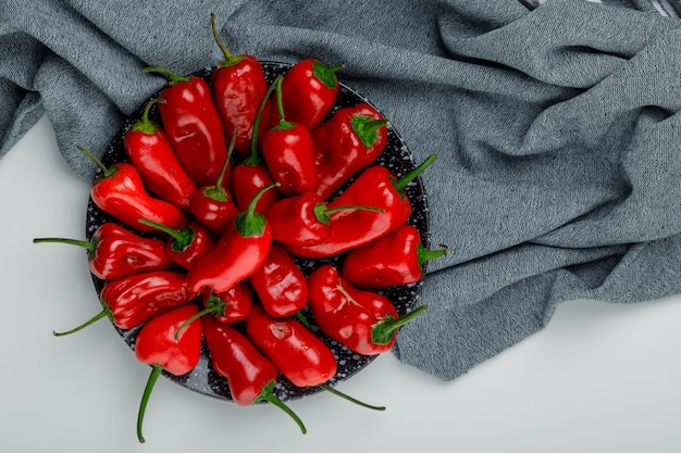 Free photo red peppers in a plate flat lay on white and textile wall
