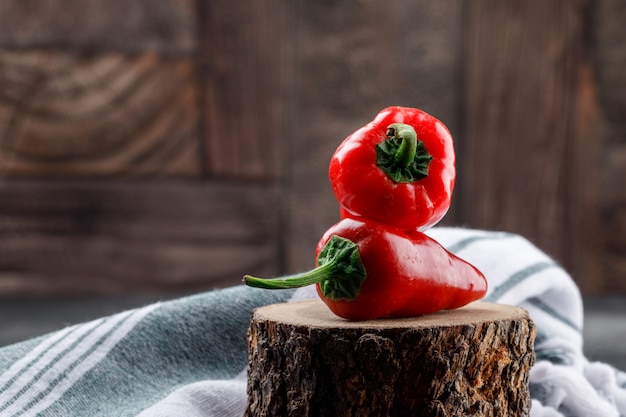 Red peppers with picnic cloth on a wooden piece on grungy and stone tile wall, side view.