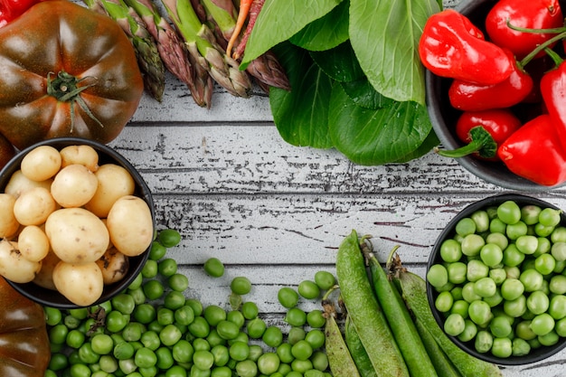 Red peppers with potatoes, tomatoes, asparagus, sorrel, green pods, peas, carrots in a bowl on wooden wall, top view.