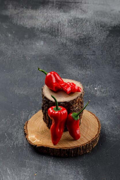 Red peppers with wooden pieces on grungy grey wall, high angle view.