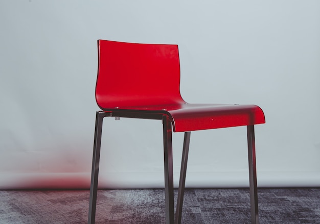 Красный пластиковый стул возле белой стены