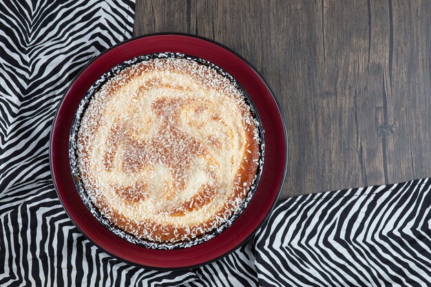 Red plate of delicious pie powdered with sugar placed on tablecloth .