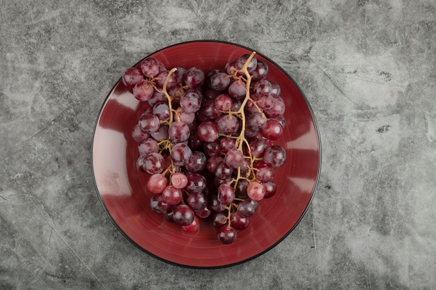 Red plate of fresh grapes placed on marble surface.