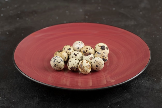 Red plate of raw fresh quail eggs on black surface.