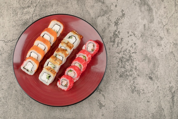 Red plate of various delicious sushi rolls on marble background
