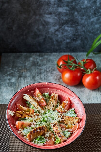 A red plate with caesar salad and tomatoes in the marble surface