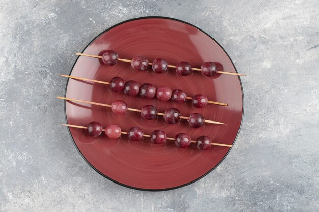 A red plate with ripe fresh grapes on a marble .