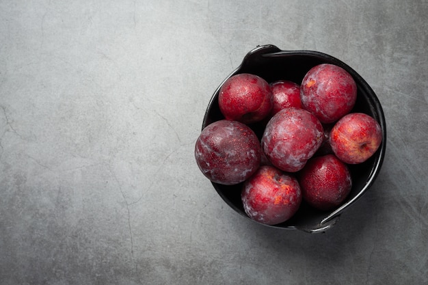 Red plum put in black bowl on dark floor