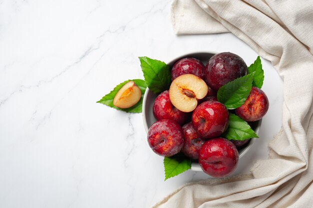 Red plum put in white bowl on white floor