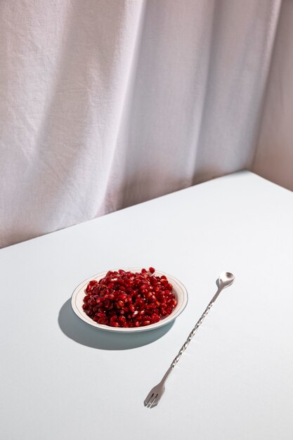 Red pomegranate seeds on plate with metal cocktail spoon over white table