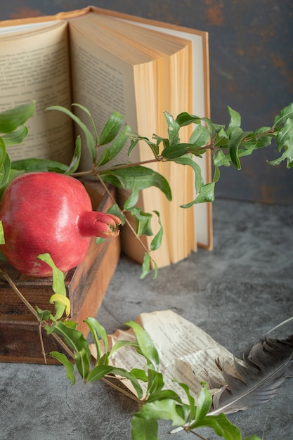 Red pomegranate in wooden box with book and leaves