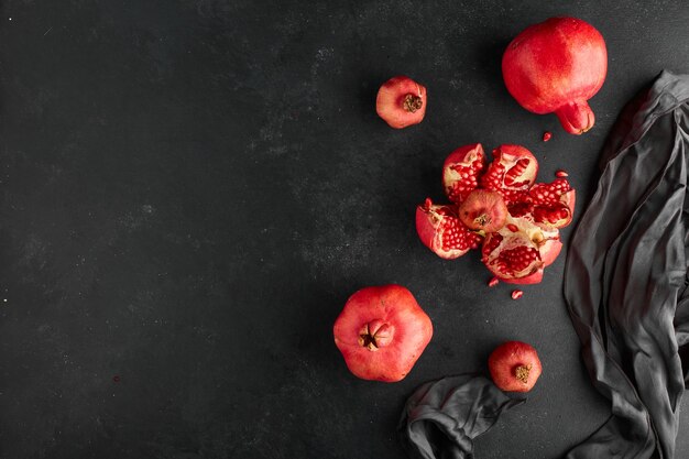 Red pomegranates on black tablecloth and surface. 