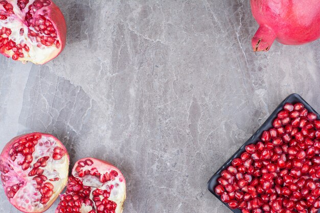 Red pomegranates and plate of seeds on stone background. 