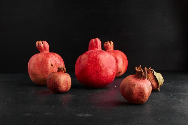 Red pomegranates in small and big shapes on black surface. 