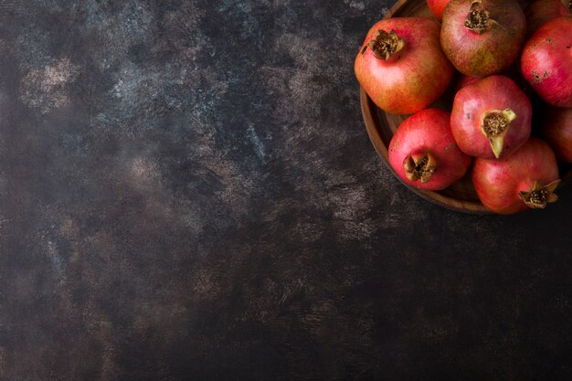 Red pomegranates in a wooden platter on marble