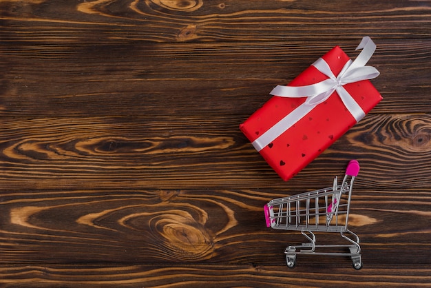 Red present box with white ribbon near shopping trolley