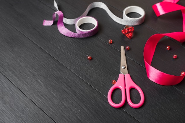 Red; purple and silver ribbons with pearls and scissor on black wooden table