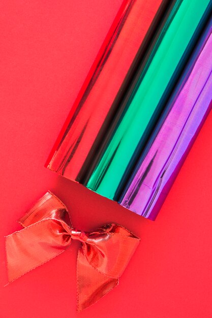 Red ribbon bow and glitter rolled up paper on red background