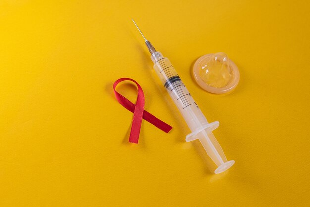 Red ribbon latex condom and syringe on the blue table