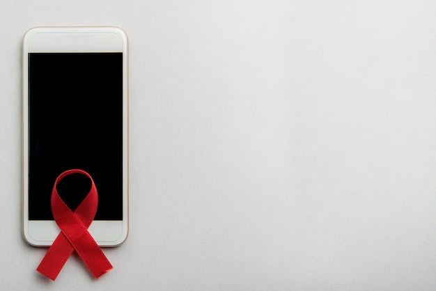 Foto gratuita nastro rosso e telefono cellulare con sfondo bianco. l'hiv aiuta la consapevolezza del nastro