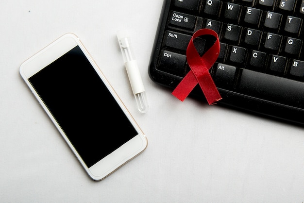 Nastro rosso e telefono cellulare con sfondo bianco. l'hiv aiuta la consapevolezza del nastro Foto Gratuite