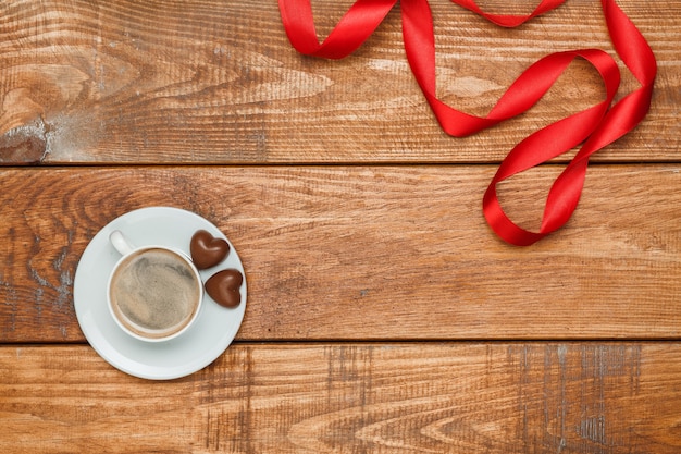 The red  ribbon, small hearts on  wooden background with a cup of coffee