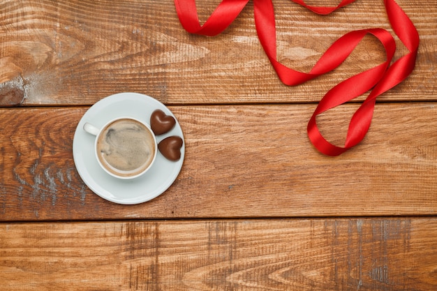 The red  ribbon, small hearts on wooden with a cup of coffee