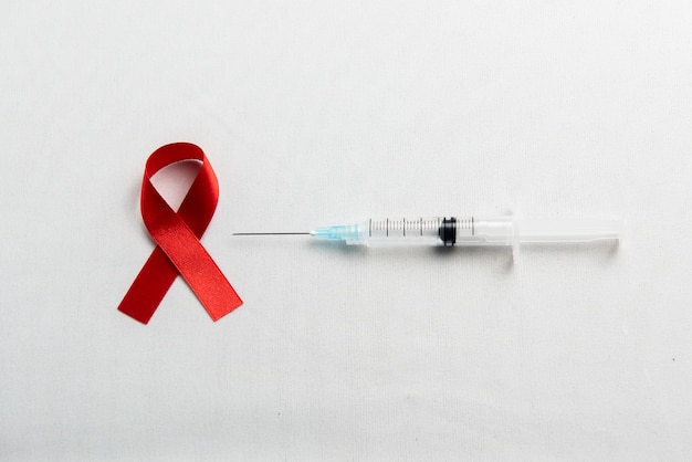 白い背景の赤いリボンと注射器。 HIVエイズリボンの認識