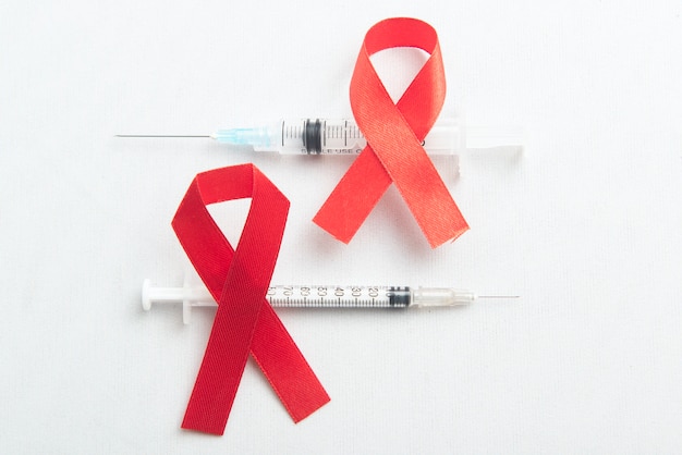 Free photo red ribbon and syringe with white background. hiv aids ribbon awareness