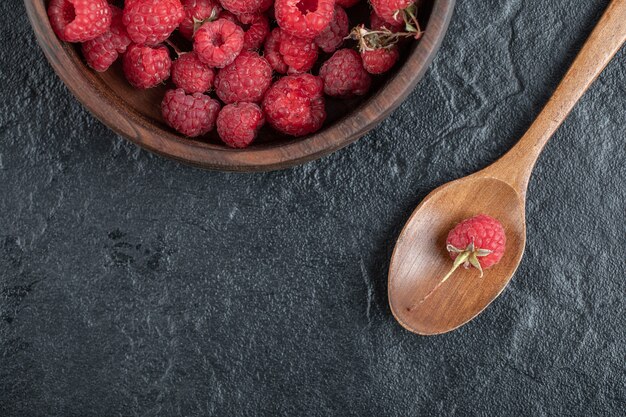 red ripe raspberries in wooden bowl on marble table