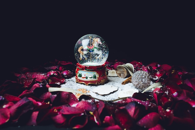 Красные лепестки роз окружают рождественский стеклянный шар со снегом