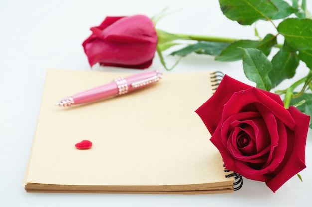 Красная роза и розовая ручка с блокнотом на белом фоне