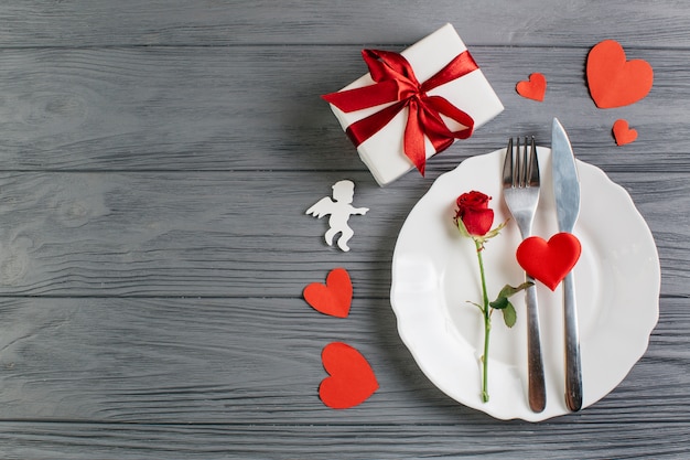 Red rose with cutlery on white plate