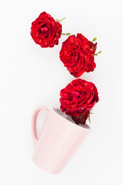 Red roses over the tilt pink mug on white background