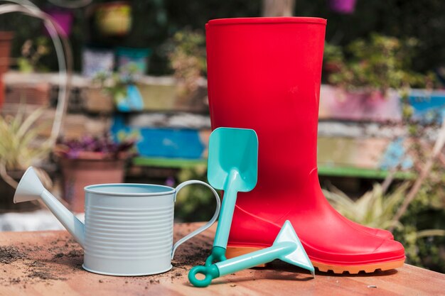 Красный резиновый чехол; синяя лопата и лейка на столе в саду