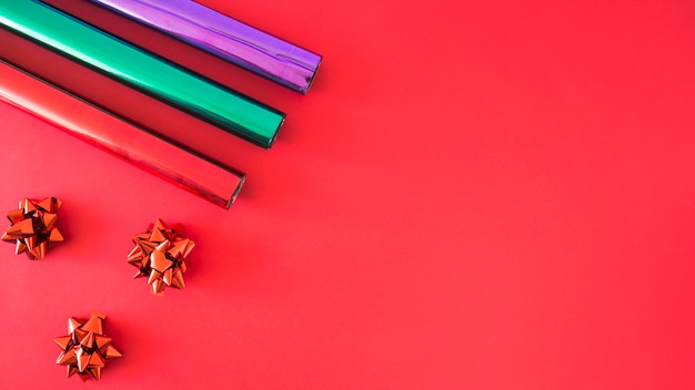 Red satin bow and three rolled up wrapping paper on red background