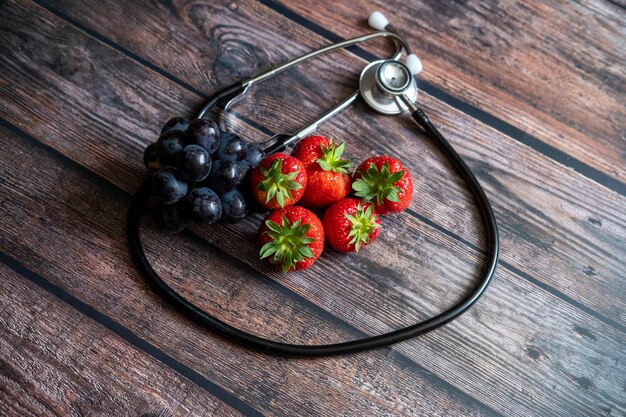 Red Scottish strawberries and black grapes with stethoscope on top of wooden table