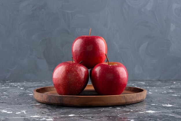 Красные блестящие целые яблоки на деревянной тарелке.