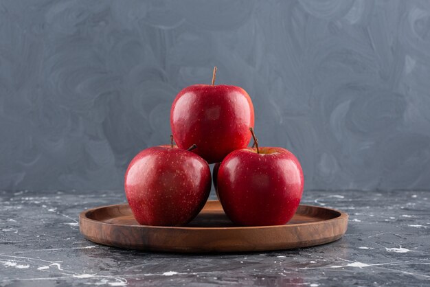 Red shiny whole apples placed on wooden plate.