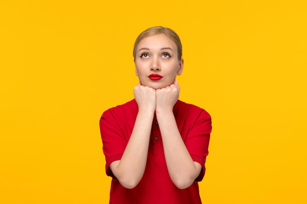 Red shirt day blonde girl looking up fists under chin in a red shirt on a yellow background