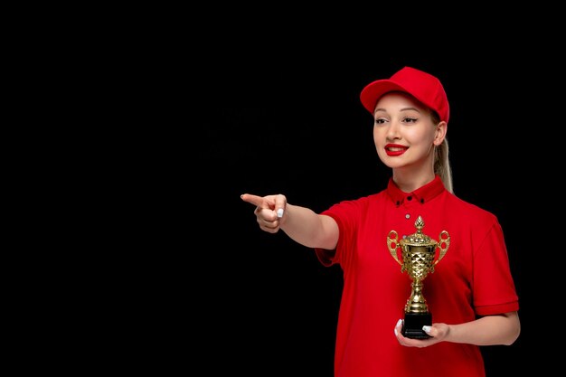 Red shirt day happy girl pointing front with trophy in red cap wearing shirt and bright lipstick