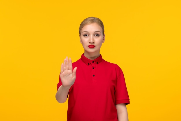 Red shirt day pretty woman showing stop gesture in a red shirt on a yellow background