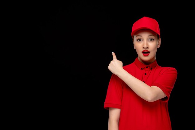 シャツと明るい口紅を身に着けている赤い帽子で後ろを指している赤いシャツの日驚いた女の子