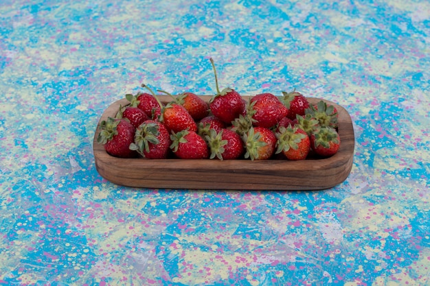 Бесплатное фото Красная клубника в деревянном блюде на синем столе