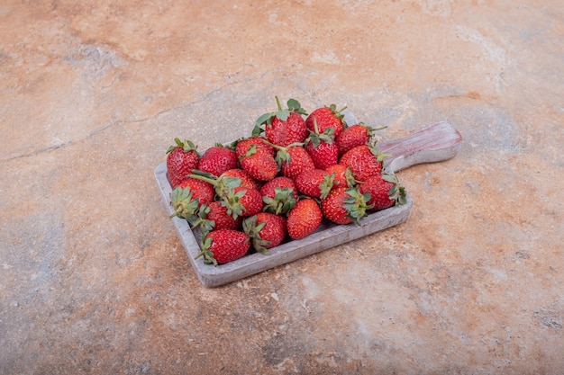 Red strawberries in a rustic wooden platter on the marble